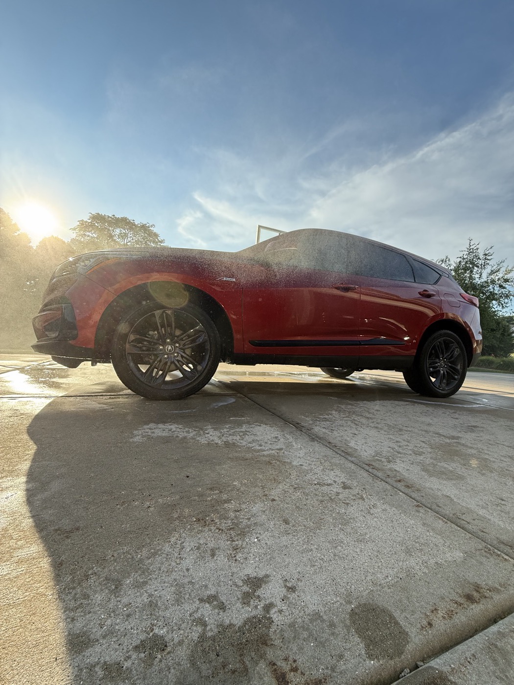 Red Acura SUV side profile mid-wash, soap suds on the paint, golden hour light