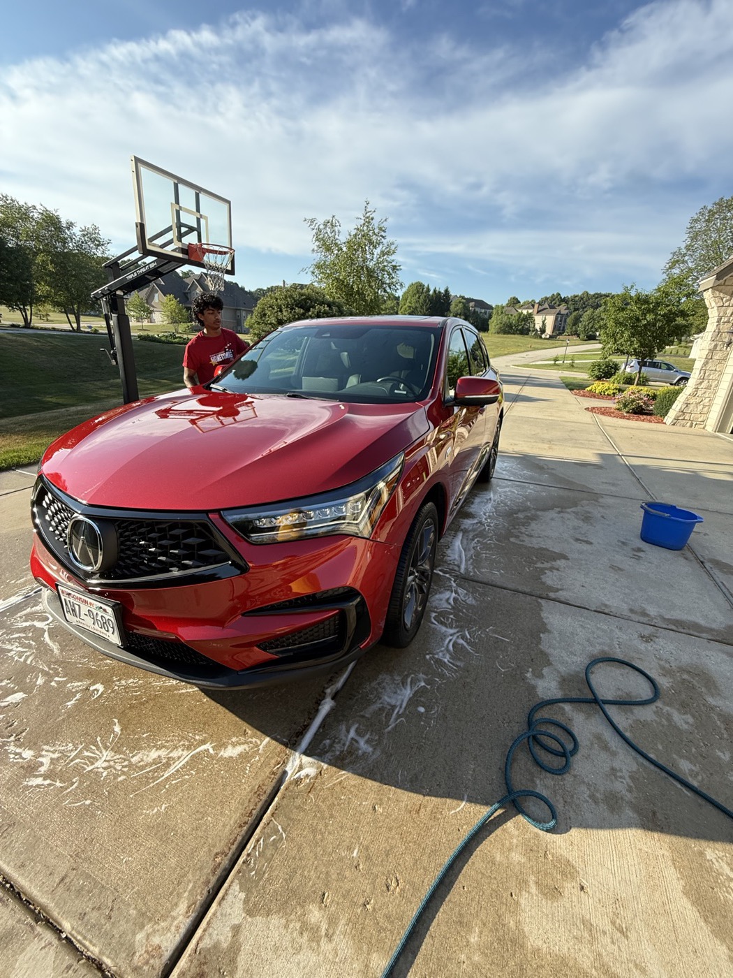 Red Acura RDX front three-quarter view mid-detail, soap suds on driveway, Acura badge visible