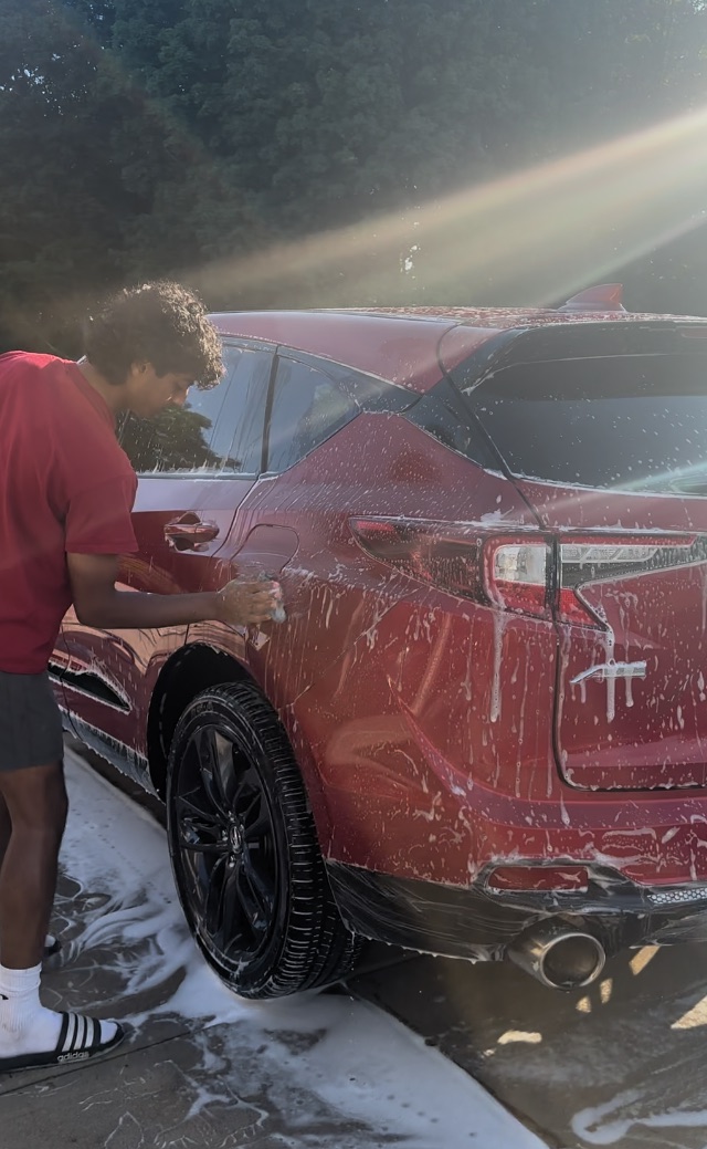 Red SUV mid-wash, foam covering the rear panels while a detailer works
